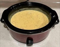 a crock pot filled with soup sitting on top of a white counter next to a black lid