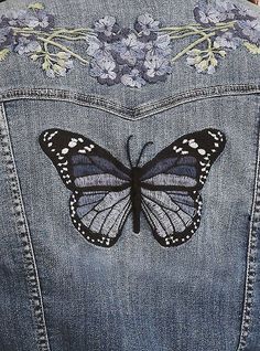 a butterfly is on the back of a jean jacket with floral appliques