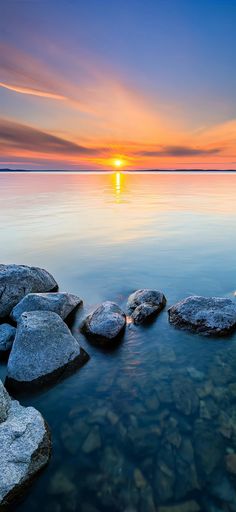 the sun is setting over some rocks in the water