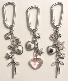 three metal keychains with charms attached to them on a white surface, one has a heart and the other has a bow