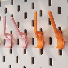 three orange and one pink hooks on a white pegboard with holes in the wall