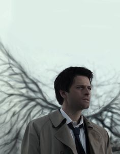 a man in a trench coat and tie standing next to a tree with no leaves