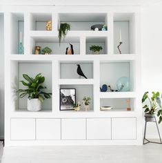 a living room filled with lots of white shelves covered in plants and potted plants