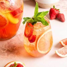 two glasses filled with lemonade and strawberries next to sliced grapefruits