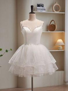 a white dress on a mannequin stand in front of a book shelf and vase