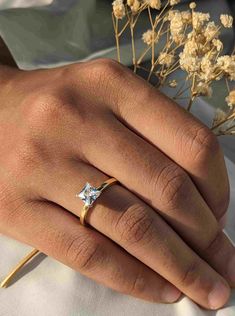 a woman's hand with a yellow gold ring on it and flowers in the background