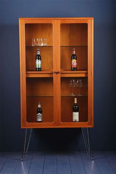 a wooden cabinet with two wine glasses and bottles on the bottom shelf, in front of a blue wall