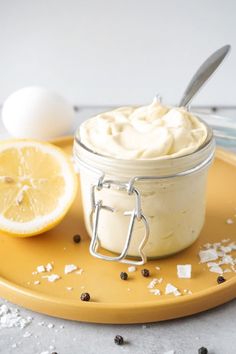 a jar filled with whipped cream next to an egg and sliced lemon on a yellow plate