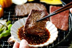 a person holding chopsticks over some meat on a grill with other food items