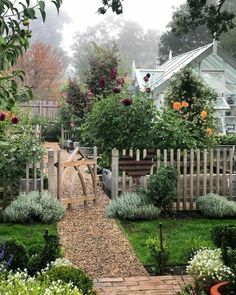 a garden with lots of plants and flowers around it, including roses on the fence