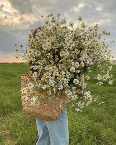 a person standing in a field holding a basket full of daisies and wildflowers