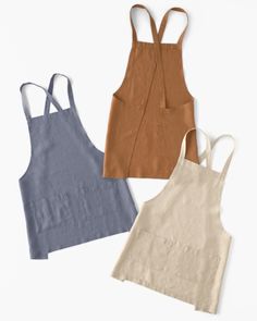 three aprons are lined up next to each other on a white surface, one is blue and the other has brown