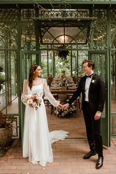 a bride and groom holding hands in front of a glasshouse at their wedding reception