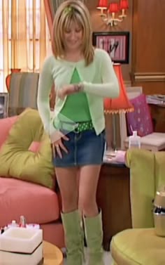 the young woman is standing in her living room wearing boots and a green shirt with an arrow on it's chest