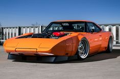 an orange sports car parked in front of a white fence with its hood up and engine on