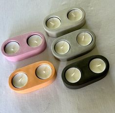 four different colored candles sitting next to each other on a white tablecloth with one candle in the middle