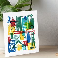 a card with an abstract cityscape design on it, sitting on a table next to a potted plant