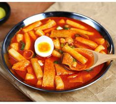 a metal bowl filled with pasta and an egg on top of it next to a wooden spoon