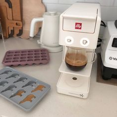 a coffee maker sitting on top of a counter next to some trays and cups