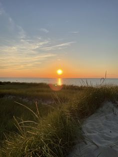 the sun is setting over the ocean and grass on the sand dunes in front of the water