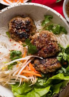 two meatballs and some veggies are in a bowl with noodles, lettuce and carrots