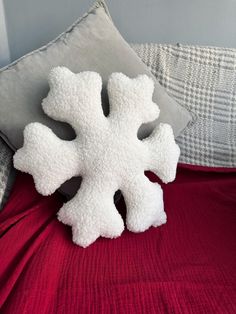 a white snowflake pillow sitting on top of a red bedspread next to pillows