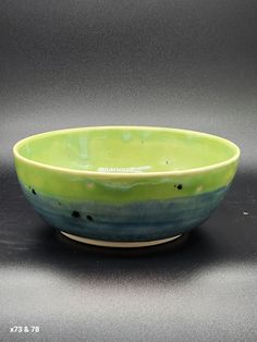 a green and blue bowl sitting on top of a table next to a gray wall