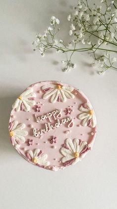 a pink birthday cake with white flowers on it and the words happy birthday written in frosting