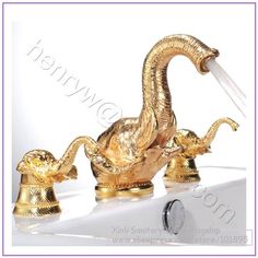 two golden swan shaped faucets on top of a sink with water coming out of them