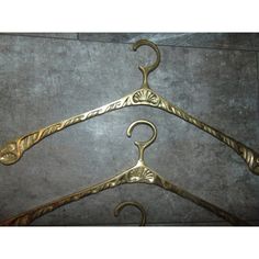 two gold colored metal hangers with ornate designs on the top and bottom, hanging from a gray wall