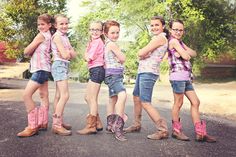 four girls in cowboy boots are standing on the road with their arms around each other