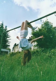 a person doing a handstand on a pole in tall grass with trees in the background