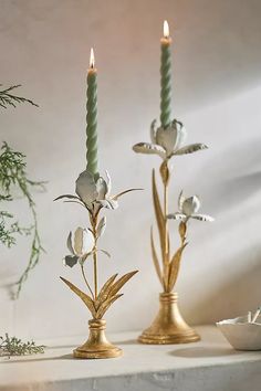 two candles that are sitting next to each other on a table with flowers and leaves