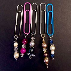 several different colored paper clips with pearls and beads hanging from them on a black surface