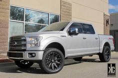 a white truck is parked in front of a building with large windows and black rims