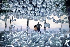 a man and woman standing in front of a large display of glass balls with cityscape in the background