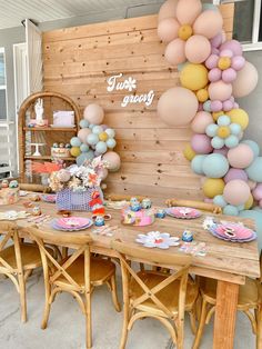 a table set up for a tea party with balloons on the wall and plates in front of it