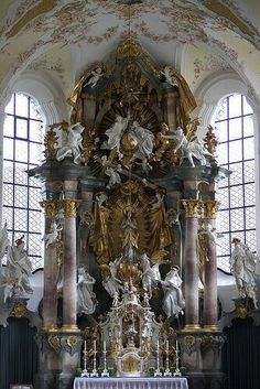 an ornate gold and white church with statues on the alter, stained glass windows in the background