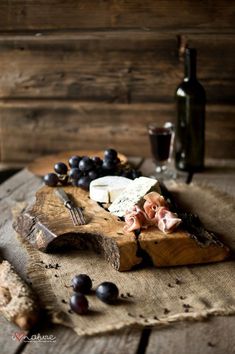 a wooden cutting board topped with meat and cheese next to a bottle of wine on top of a table