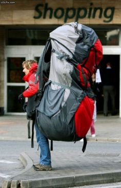 a woman carrying a large backpack on her back while walking down the street in front of a building