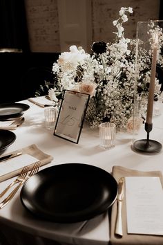 the table is set with black plates, silverware and white flowers in vases