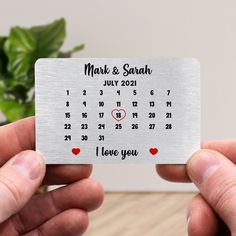 two hands holding up a metal business card with the date and heart design on it