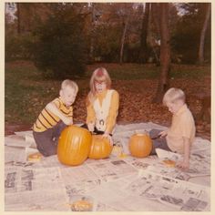 three children sitting on newspaper with pumpkins in the foreground and trees in the background