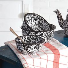 three black and white dishes sitting on top of a wooden table next to a teapot