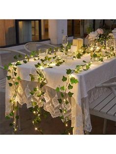 the table is covered with greenery and lite up candles for an outdoor dinner