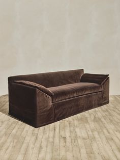 a brown velvet couch sitting on top of a wooden floor next to a white wall