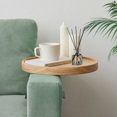 a green chair with a wooden tray on it next to a white cup and reeds