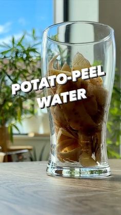 a glass filled with potato peels sitting on top of a table next to a potted plant