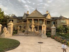 a little boy standing in front of a gated entrance to a large house with statues on it