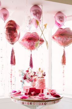 a table topped with lots of pink balloons and tassels next to a window